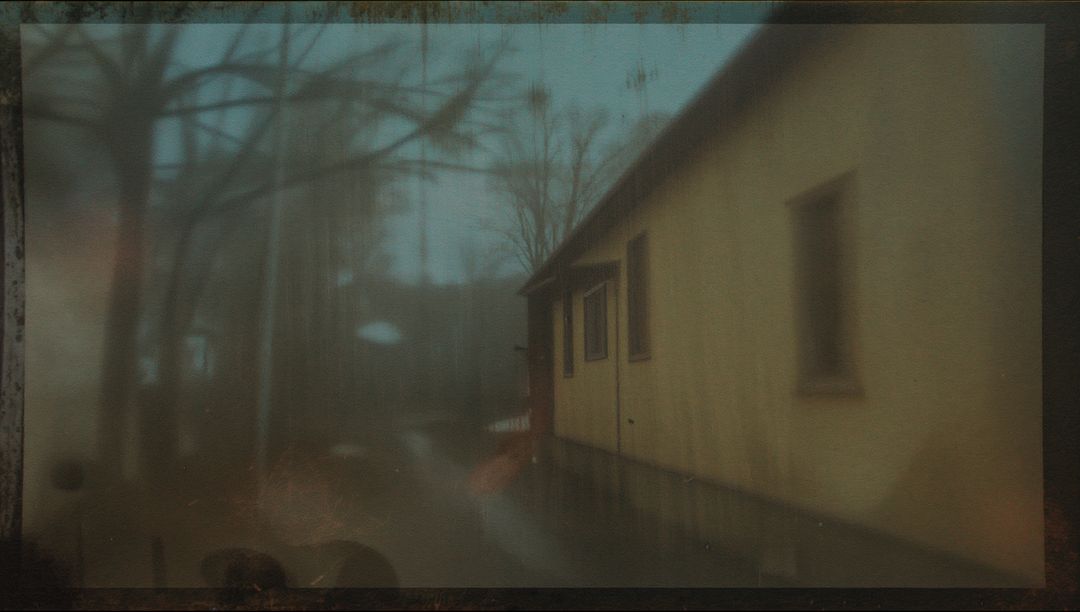 Pale windowed wall running along foggy alley with wet path, moody desaturated vignette