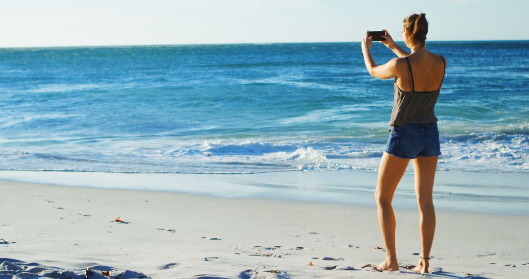 Woman Taking Photo of Ocean on Sunny Beach - Free Images, Stock Photos and Pictures on Pikwizard.com