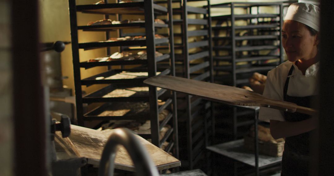 Female Baker Working in Bakery with Bread Racks in Background - Free Images, Stock Photos and Pictures on Pikwizard.com