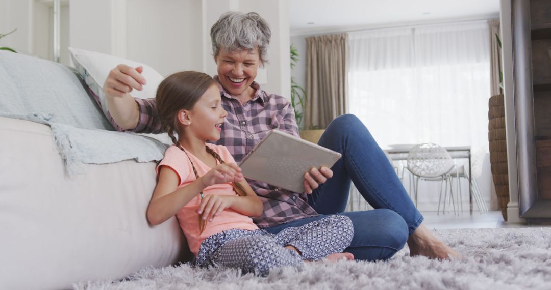 Grandmother and Granddaughter Laughing Together Using Tablet on Carpet - Free Images, Stock Photos and Pictures on Pikwizard.com