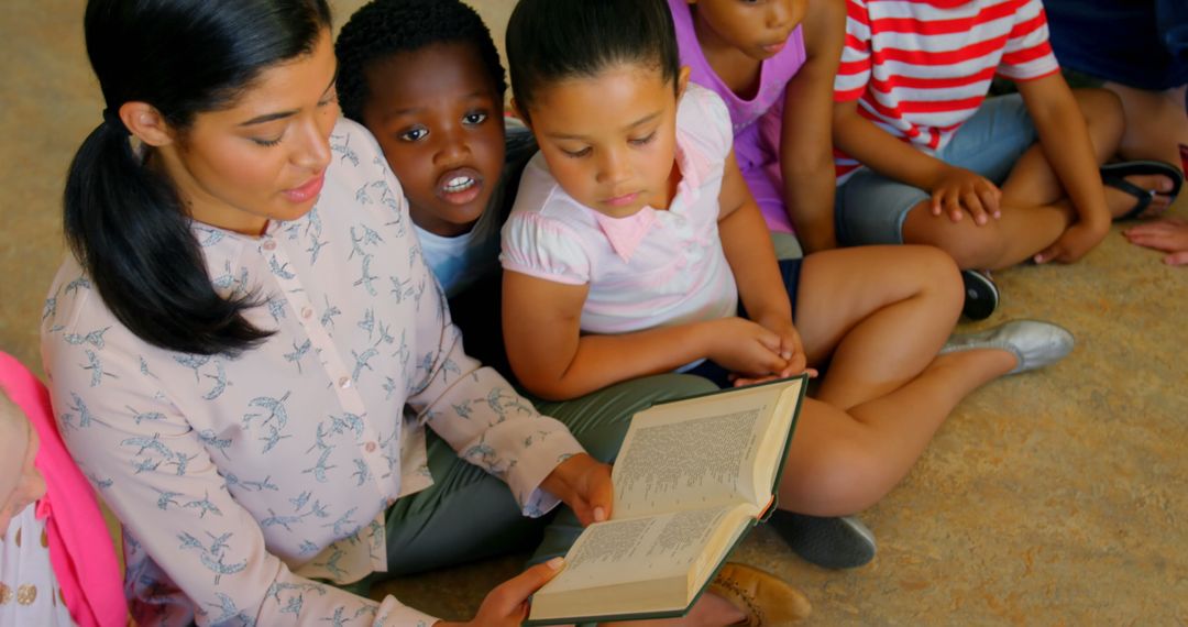 Teacher Reading Book to Attentive Schoolchildren in Classroom