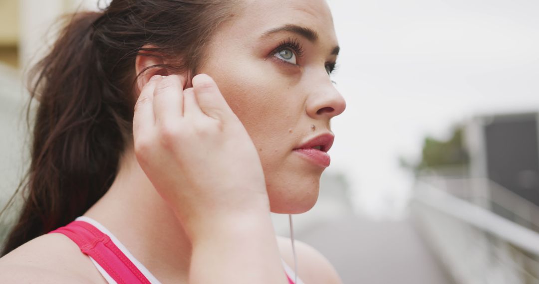 Focused Young Woman Adjusting Earbuds during Outdoor Workout - Free Images, Stock Photos and Pictures on Pikwizard.com