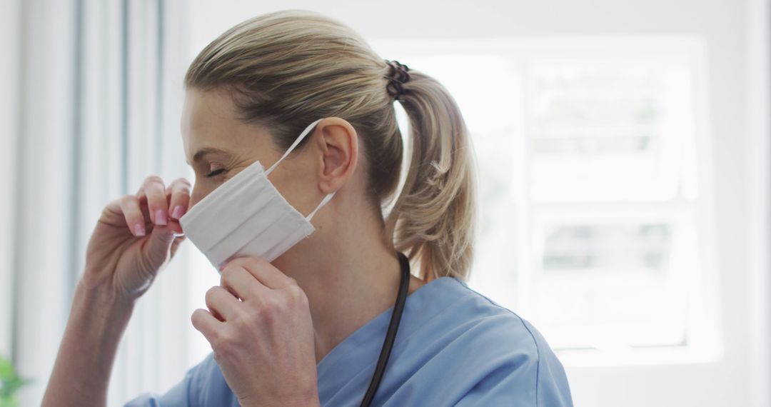 Healthcare Worker Adjusting Face Mask in Medical Facility - Free Images, Stock Photos and Pictures on Pikwizard.com