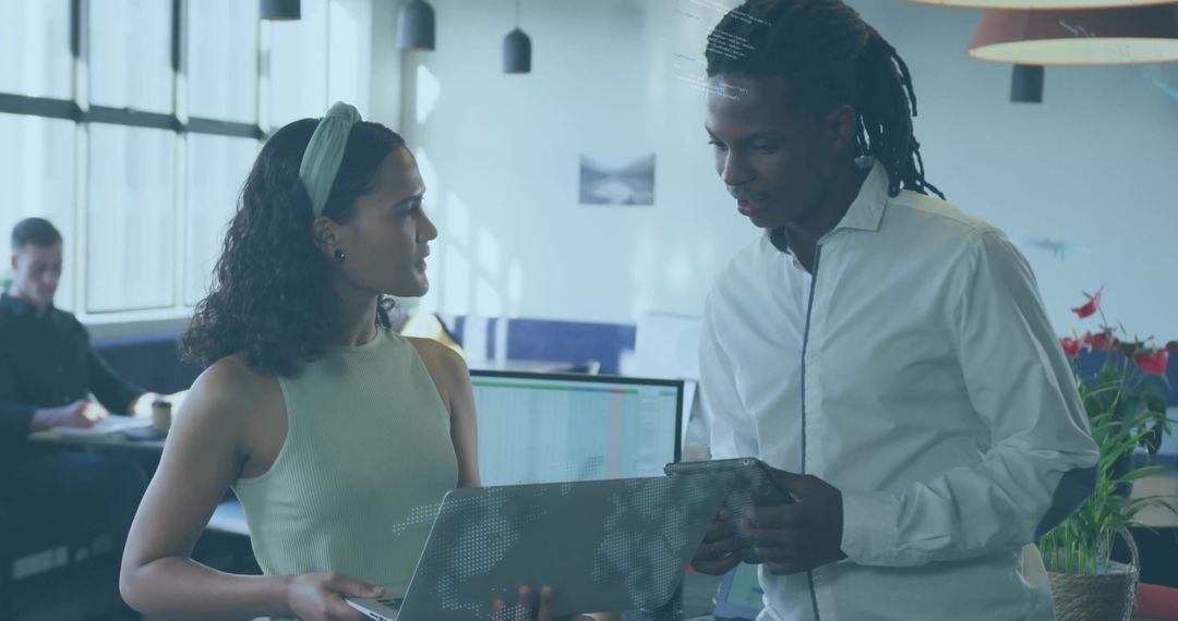 Colleagues collaborating over laptop and tablet in open office reviewing digital data