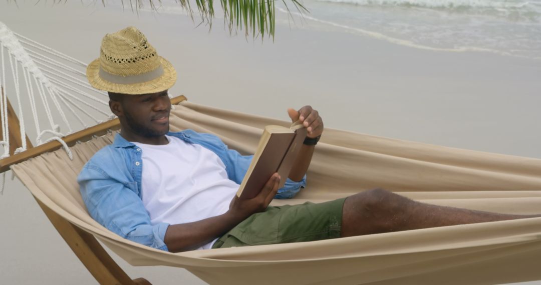 Relaxed Young Man Reading Book on Beach Hammock