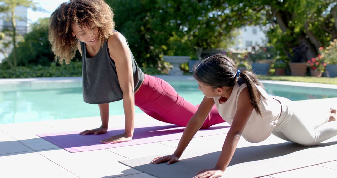 Mother and Daughter Practicing Yoga by the Pool on Sunny Day