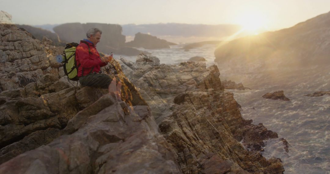 Hiker with Backpack Checking Smartphone on Coastal Rocks at Sunset