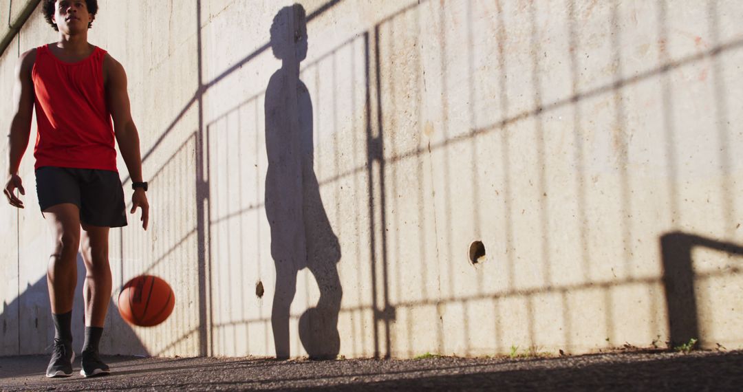 Young man dribbling basketball outside next to fence shadow - Free Images, Stock Photos and Pictures on Pikwizard.com