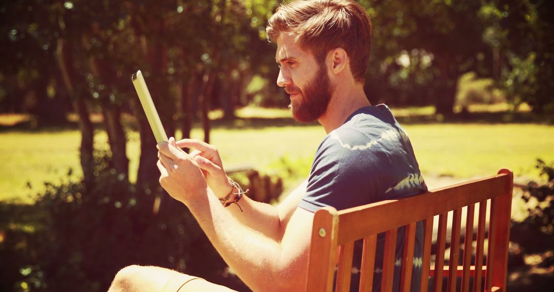 Young Man Using Tablet Outdoors in Park on a Sunny Day - Free Images, Stock Photos and Pictures on Pikwizard.com