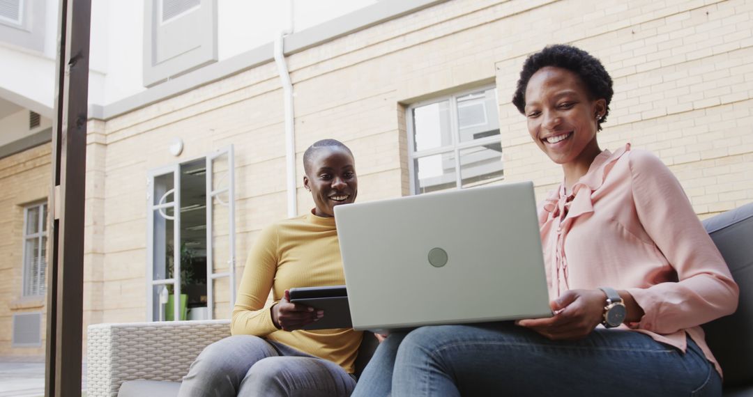 Two Women Smiling While Using Laptop and Tablet Outdoors - Free Images, Stock Photos and Pictures on Pikwizard.com