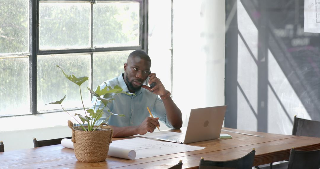 Professional Multitasking Man Using Laptop in Sunlit Office