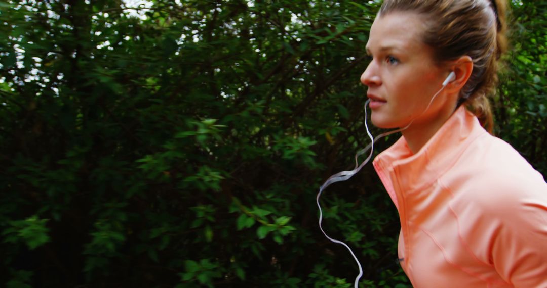 A young Caucasian woman is jogging in a lush green environment, focused and wearing earphones - Free Images, Stock Photos and Pictures on Pikwizard.com
