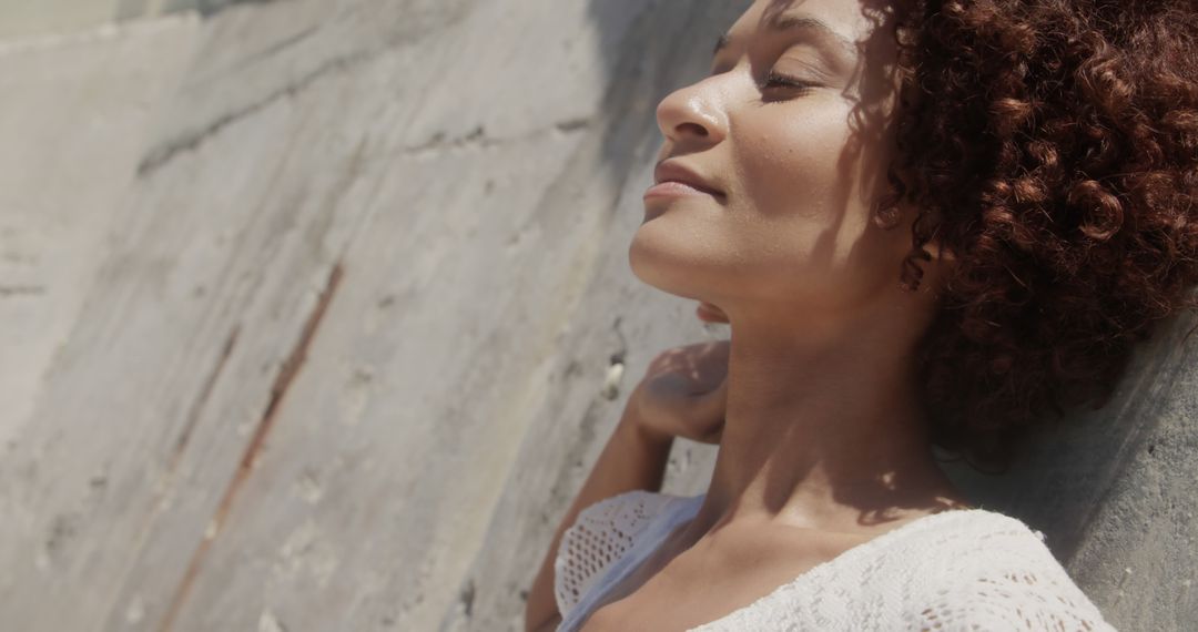 Peaceful Woman Relaxing Against Wall in Sunlight - Free Images, Stock Photos and Pictures on Pikwizard.com