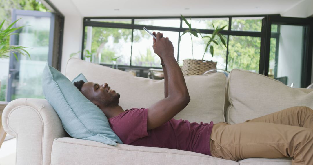 Relaxed Man Using Smartphone While Lying on Sofa in Modern Living Room - Free Images, Stock Photos and Pictures on Pikwizard.com