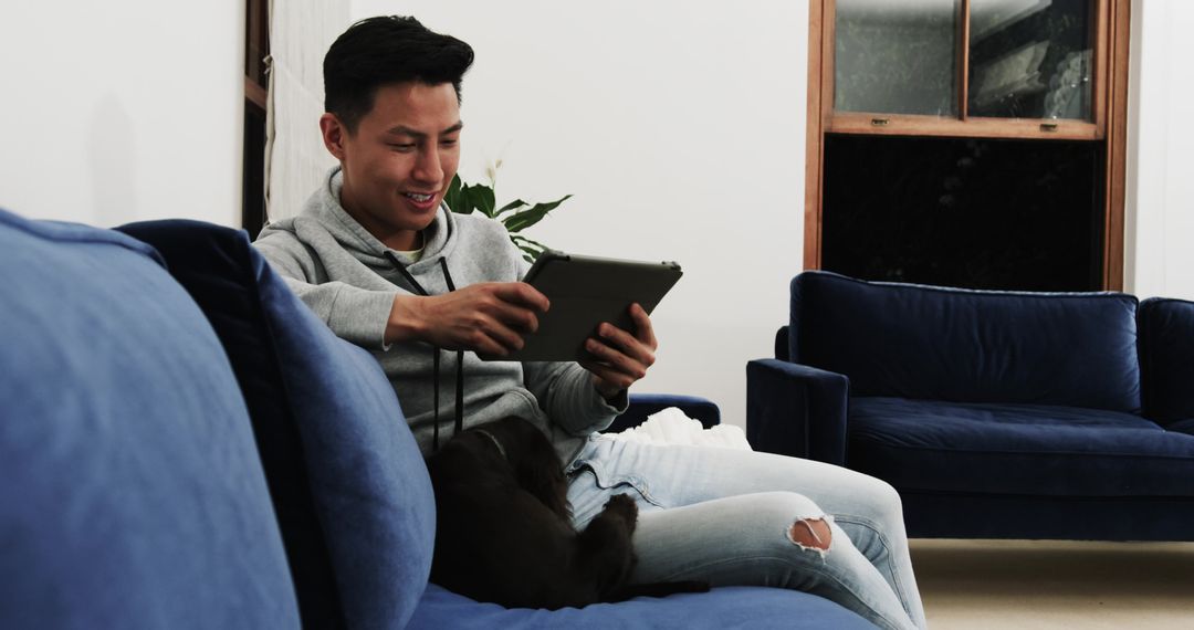 Asian Man Relaxing at Home with Tablet and Dog