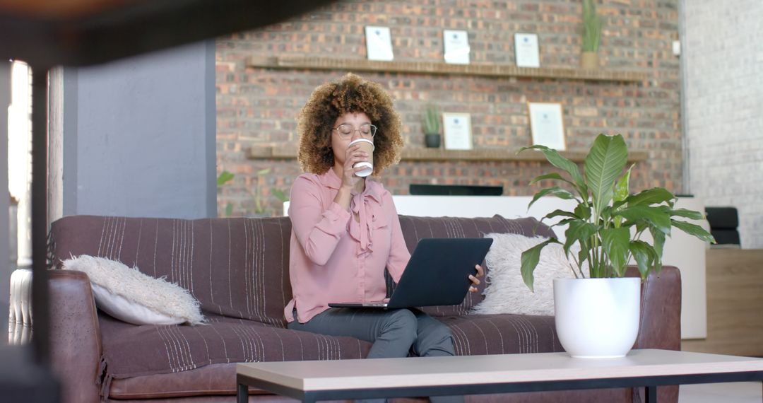 Afro-American Woman Working on Laptop and Drinking Coffee in Modern Workspace - Free Images, Stock Photos and Pictures on Pikwizard.com