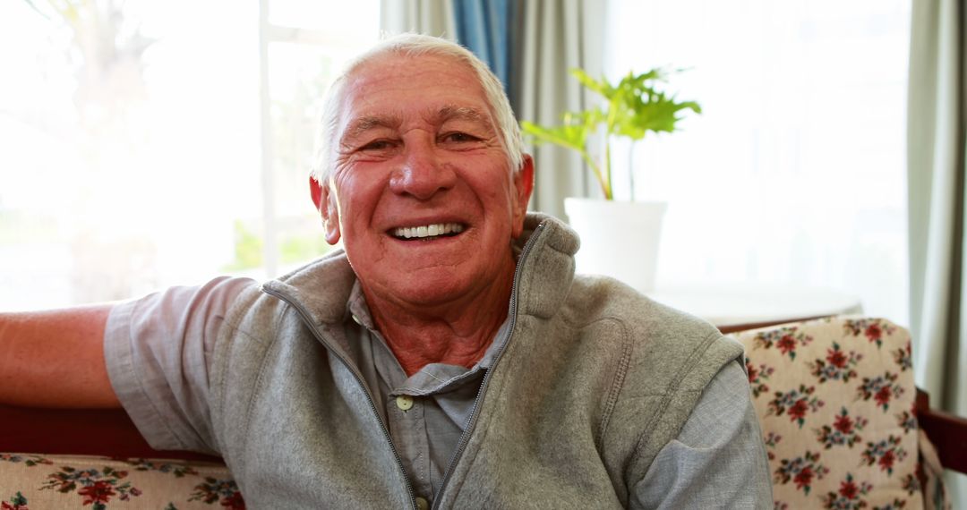 Elderly man sitting on couch smiling at home - Free Images, Stock Photos and Pictures on Pikwizard.com