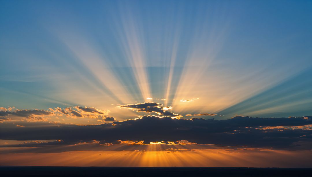 Sunburst Radiating Through Layered Clouds Casting Crepuscular Rays Over Vast Plain