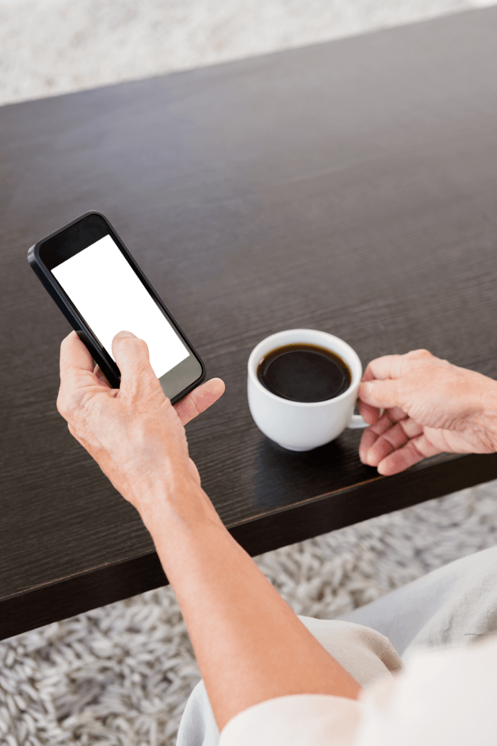 Senior Adult Holding Smartphone and Coffee on Dark Table