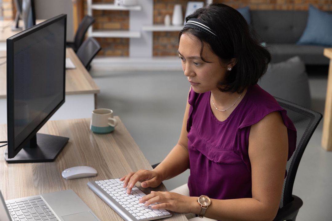 Asian Woman Typing at Desk in Modern Office Space
