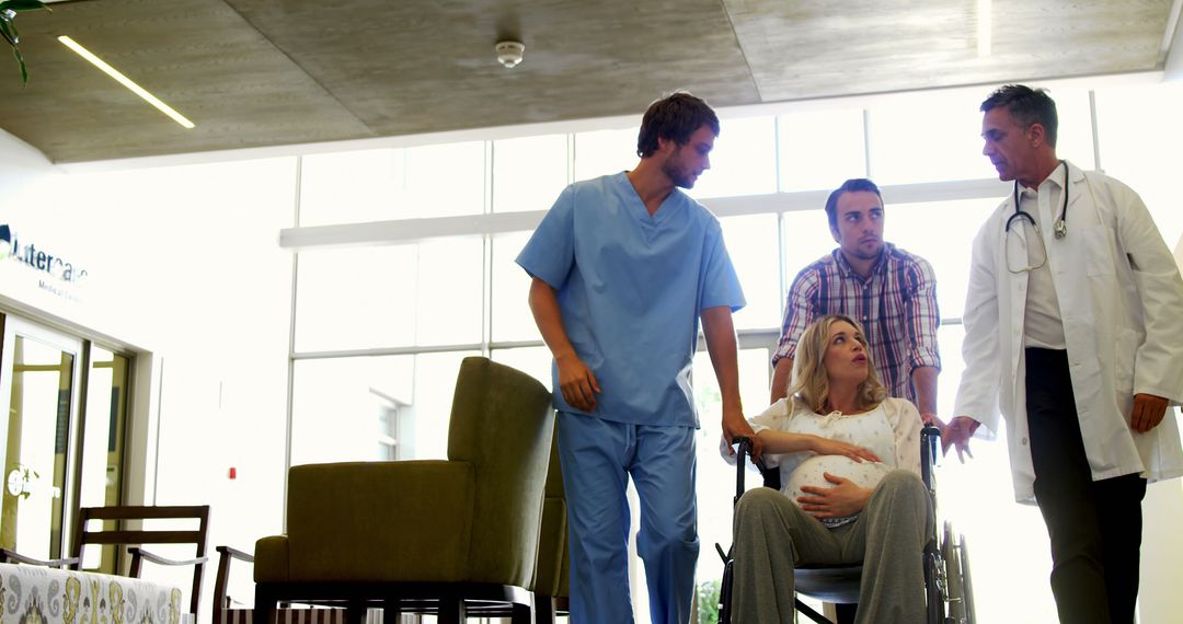 Pregnant Woman in Wheelchair Accompanied by Medical and Support Staff in Hospital - Free Images, Stock Photos and Pictures on Pikwizard.com