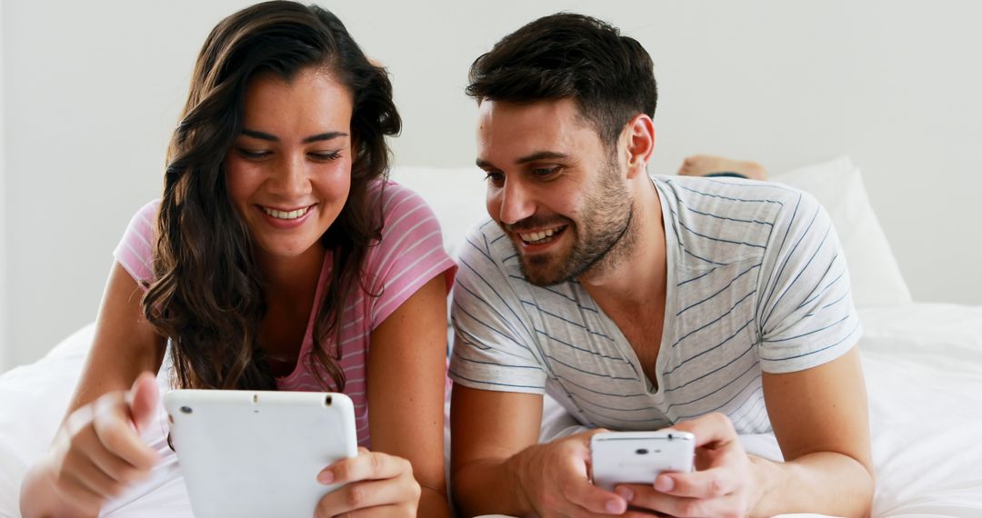 Happy Couple Relaxing in Bed Using Tablet and Smartphone