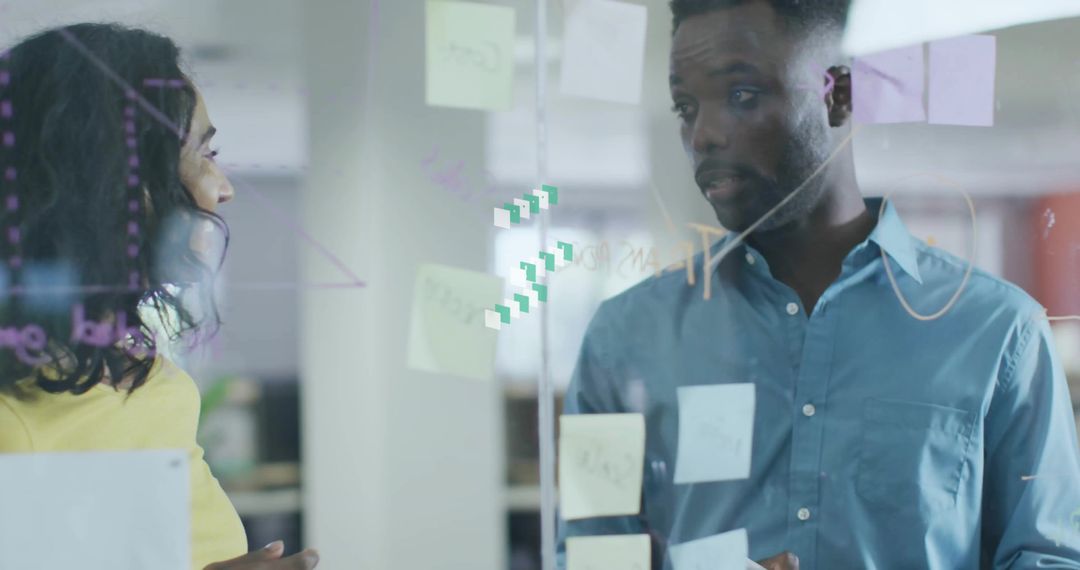 Coworkers collaborating at glass board with sticky notes and diagrams in modern office