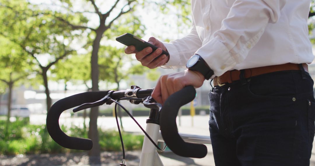 Businessman Checking Smartphone While Holding Bicycle Handlebars in Park - Free Images, Stock Photos and Pictures on Pikwizard.com