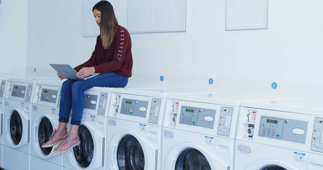 Young Woman Using Laptop While Sitting on Washing Machines in Laundromat - Free Images, Stock Photos and Pictures on Pikwizard.com