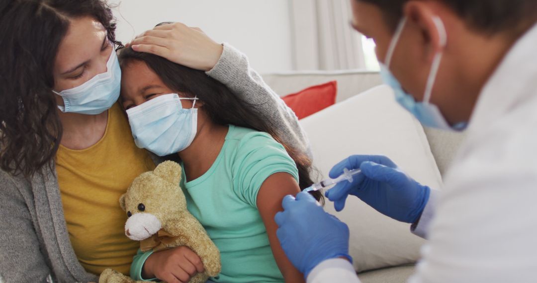 Hispanic male doctor making injection to girl with mother at home, all wearing face masks, - Free Images, Stock Photos and Pictures on Pikwizard.com