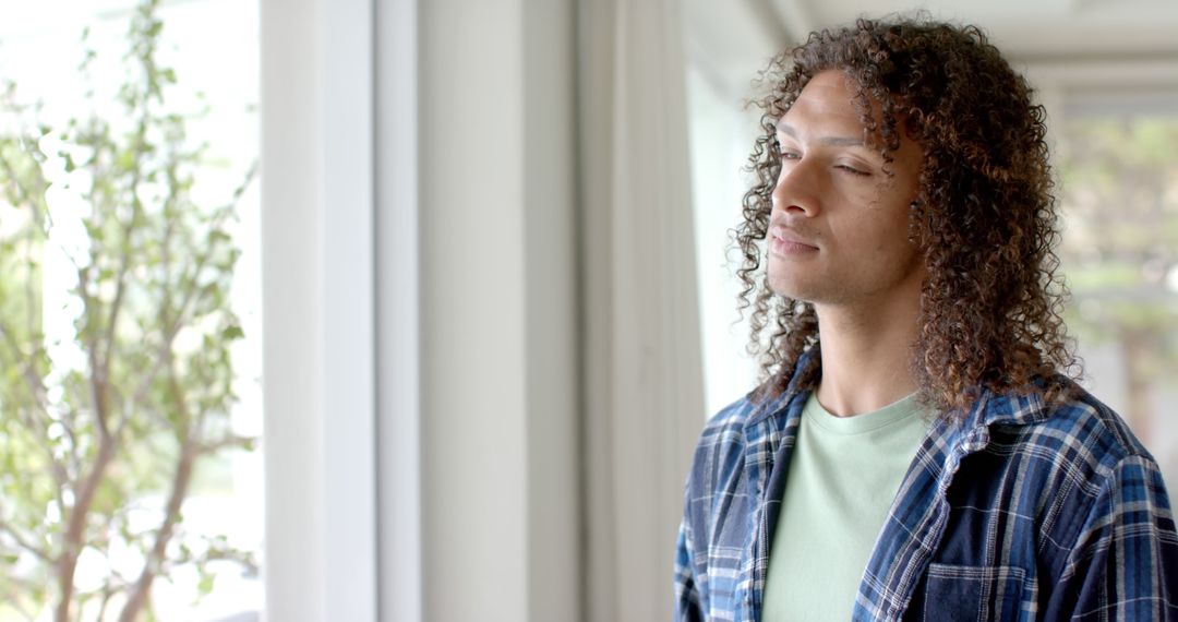 Young Man with Curly Hair Enjoying Peaceful Moment By Window - Free Images, Stock Photos and Pictures on Pikwizard.com