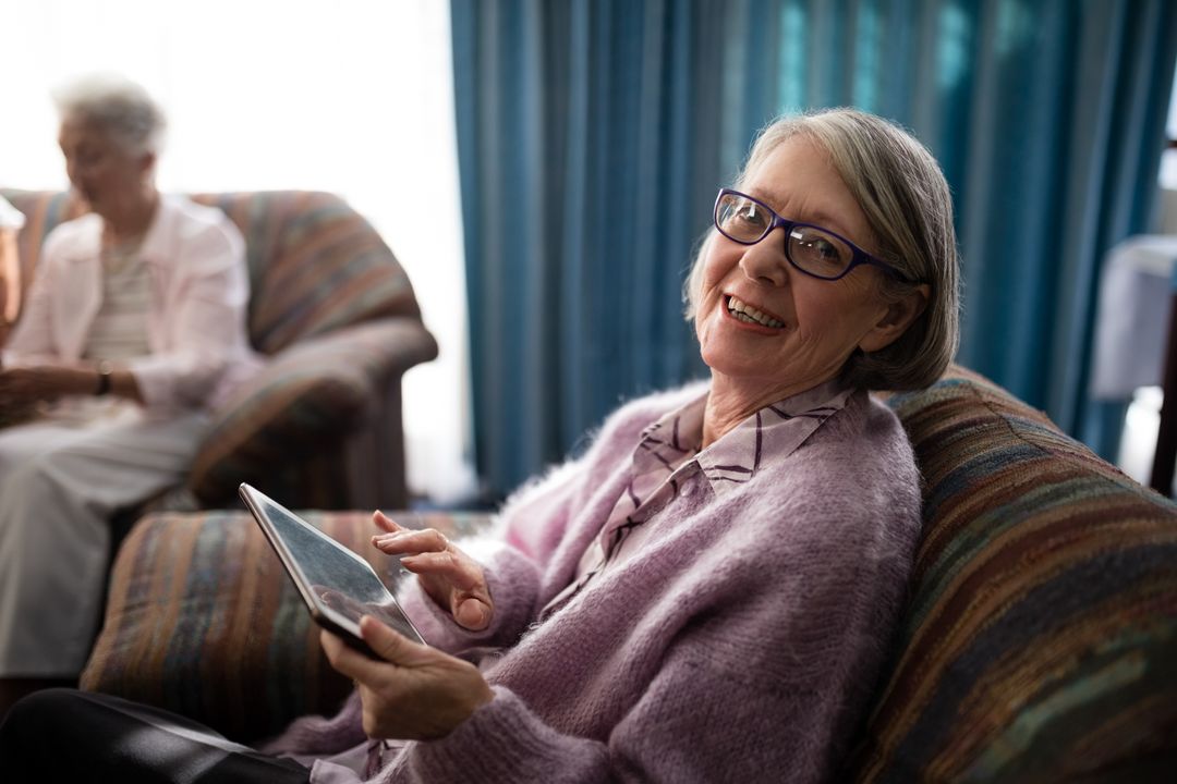 Portrait of smiling senior woman sitting with digital tablet on armchair - Free Images, Stock Photos and Pictures on Pikwizard.com