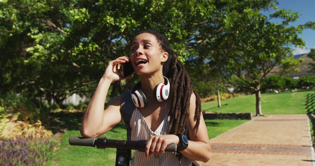 Young Woman with Dreadlocks Talking on Phone While Riding Scooter in Park - Free Images, Stock Photos and Pictures on Pikwizard.com