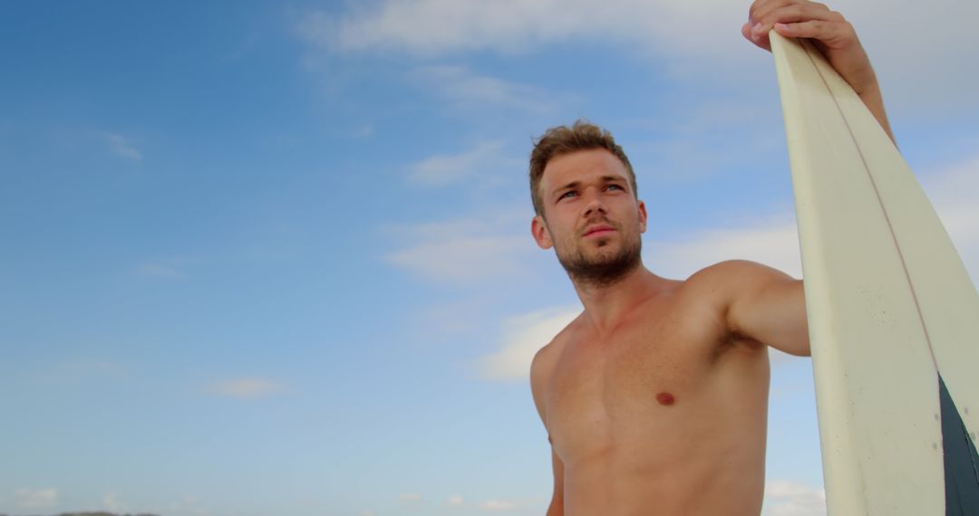 Confident Surfer Standing with Surfboard against Blue Sky