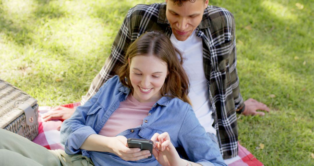 Happy Couple Enjoying Picnic with Smartphone in Sunny Garden