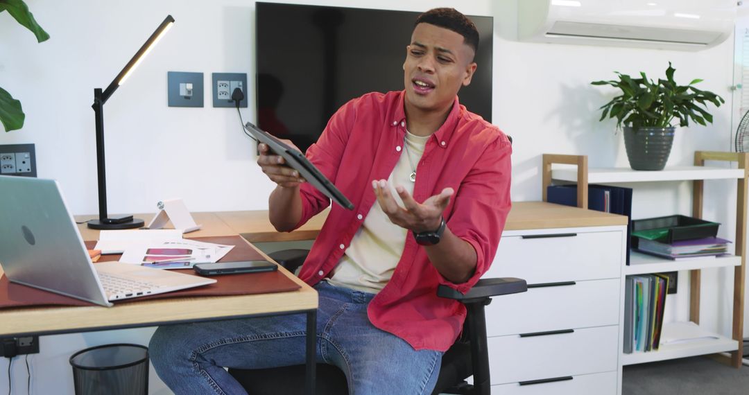 Frustrated Man Holding Tablet in Modern Office with Earbuds