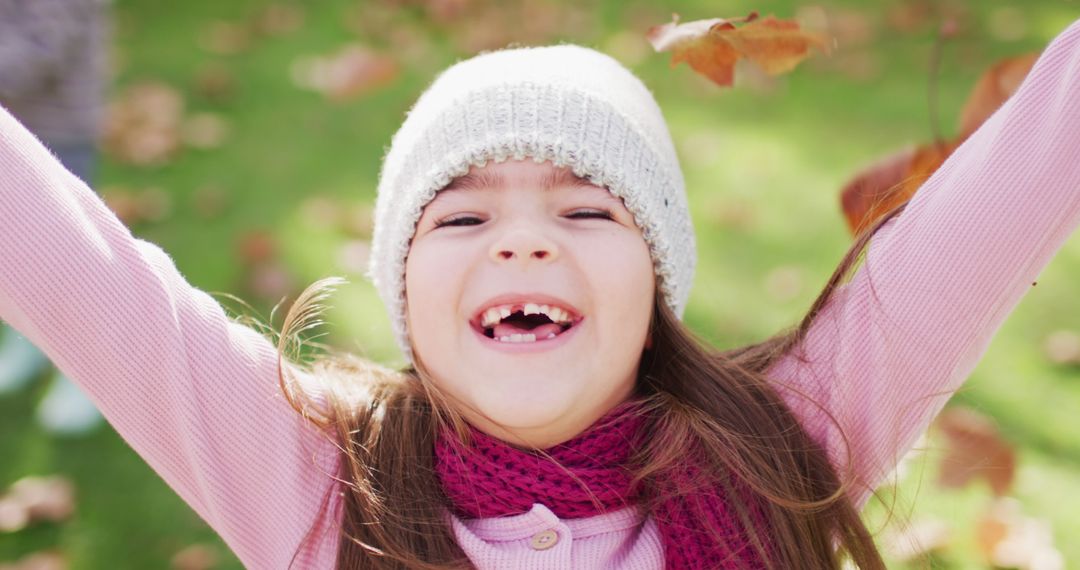 Image of happy caucasian girl in woolly hat and scarf throwing autumn leaves in garden - Free Images, Stock Photos and Pictures on Pikwizard.com