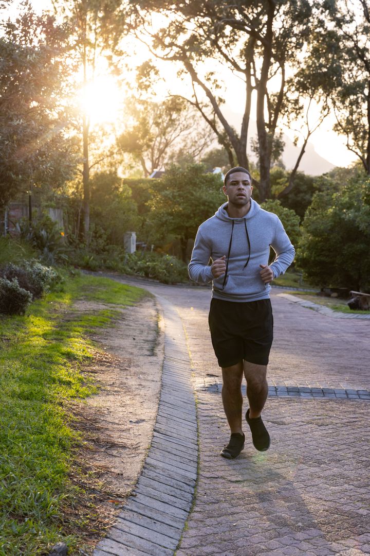 Man Jogging on Path Amidst Sunrise in Suburban Park