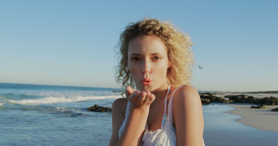 Young Woman Blowing Kiss on Sunny Beach at Sunset - Free Images, Stock Photos and Pictures on Pikwizard.com