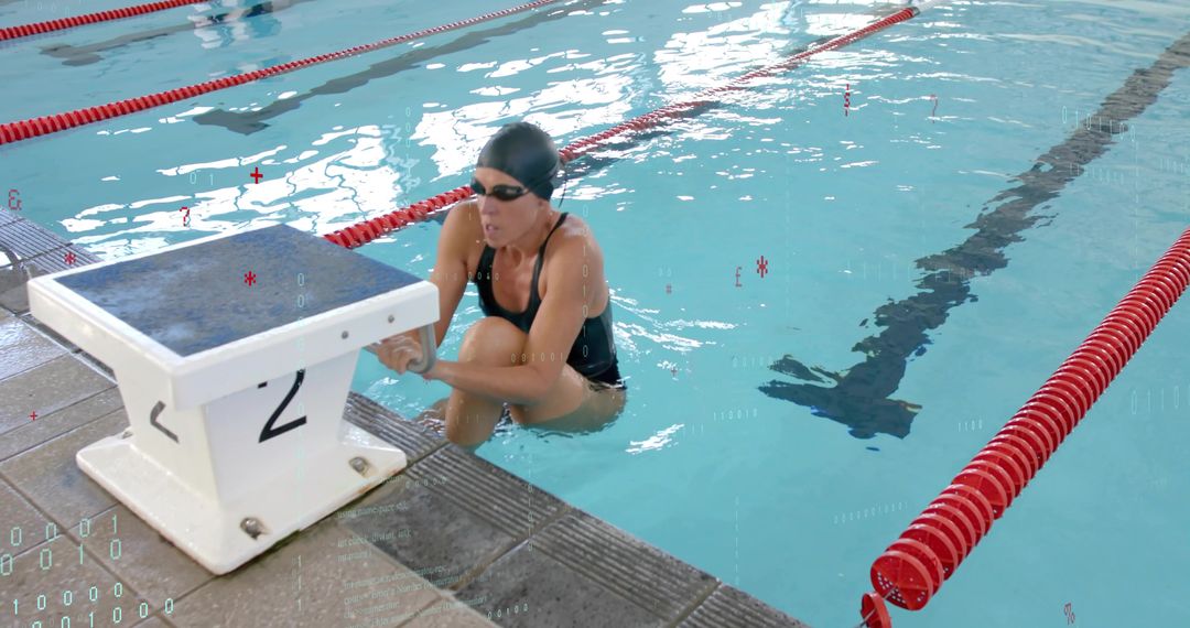 Competitive swimmer bracing on starting block 2 in indoor lap pool