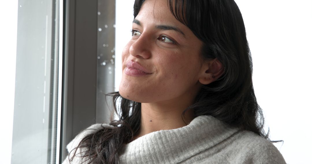 Woman Contemplates by Rain-Speckled Window in Minimalistic Setting