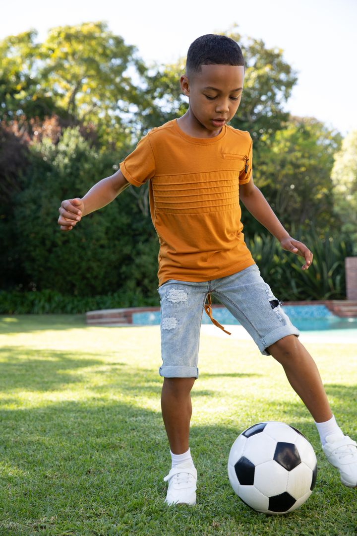 Young Boy Having Fun Playing Soccer On Sunny Lawn