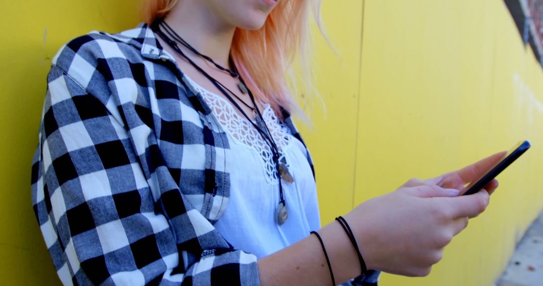 Young Woman Using Smartphone Against Yellow Wall - Free Images, Stock Photos and Pictures on Pikwizard.com