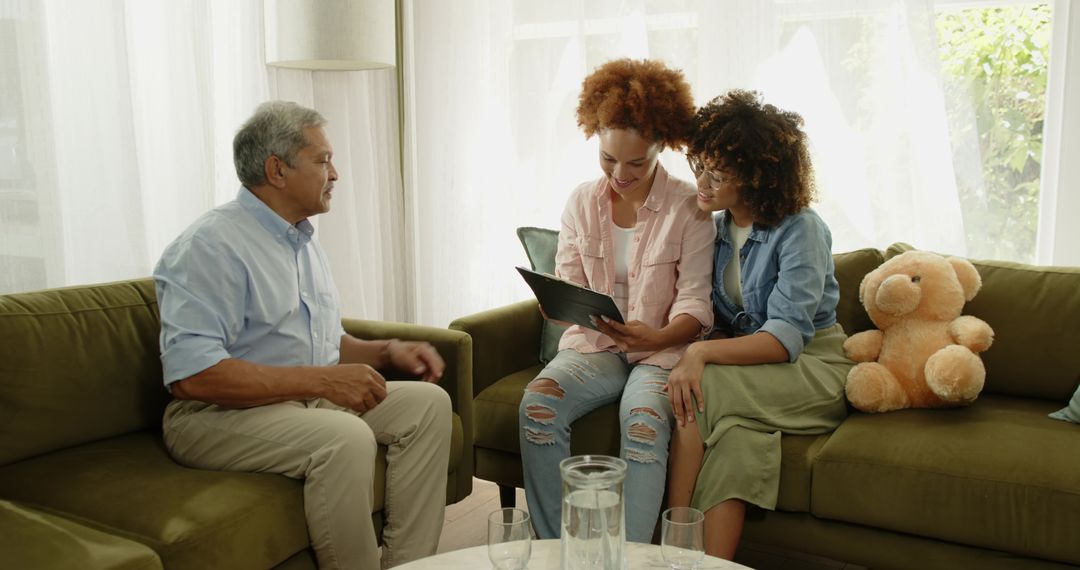 Multigenerational family sharing tablet, smiling and chatting on olive-green sofa at home