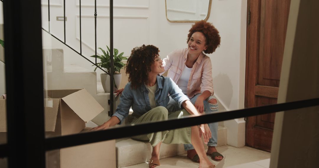 Friends unpacking and laughing on stair landing during sunny move-in in cozy home foyer