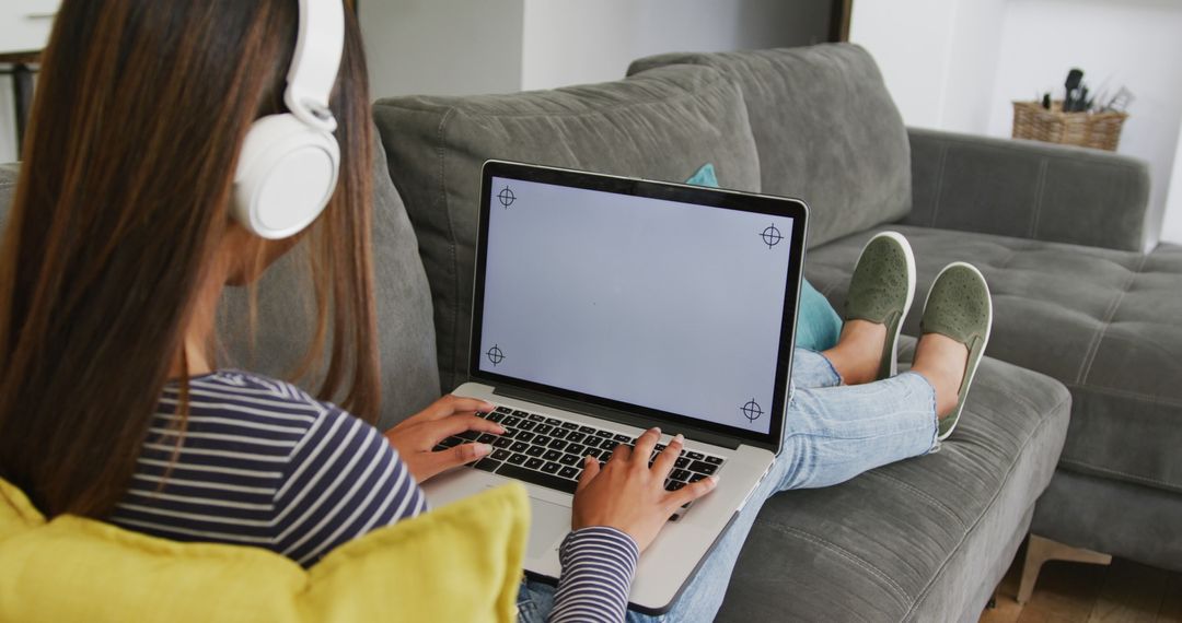 Woman Sitting Comfortably on Sofa Using Laptop with Headphones - Free Images, Stock Photos and Pictures on Pikwizard.com