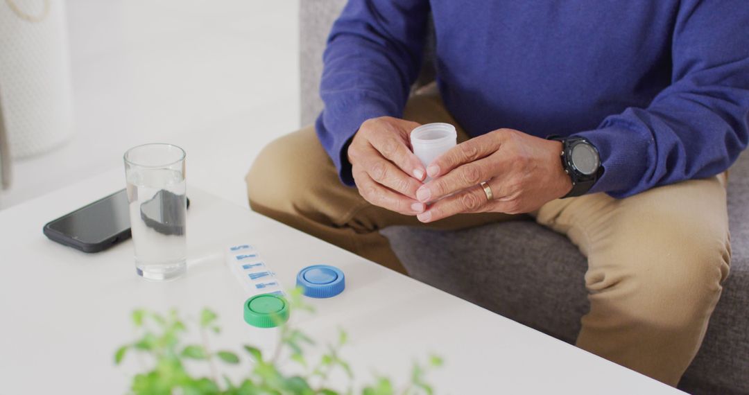 Image of midsection of senior biracial man sitting and taking pills at home - Free Images, Stock Photos and Pictures on Pikwizard.com