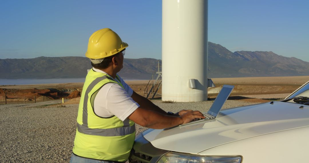 Engineer with Laptop Inspecting Wind Turbine in Rural Landscape