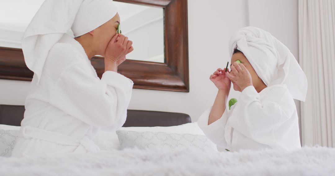 Image of happy asian mother and daughter in robes doing cucumber mask and having fun - Free Images, Stock Photos and Pictures on Pikwizard.com