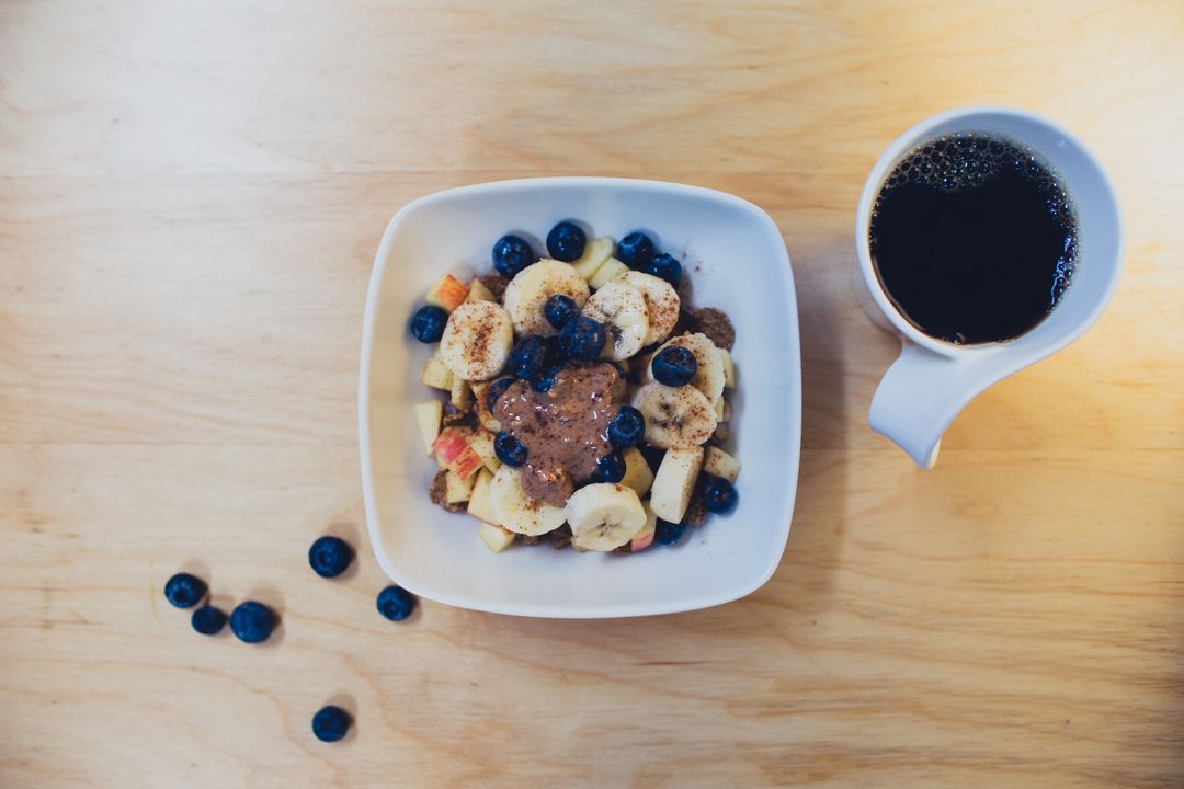 Serving colorful healthy granola breakfast bowl with banana, blueberries, apple and coffee